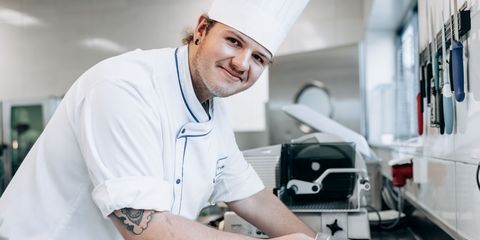 junger Koch steht lachend in der Küche vor Schneidebrett