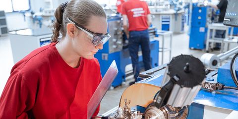 Auszubildende steht mit Schutzbrille an mechanischer Maschine in der Akademie