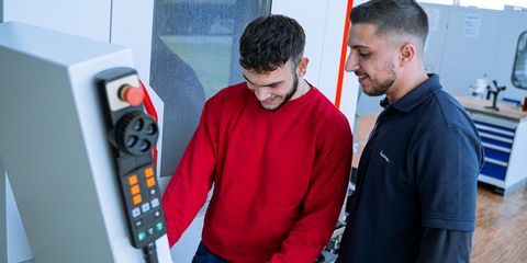 Azubi und Ausbilder stehen an CNC Maschine