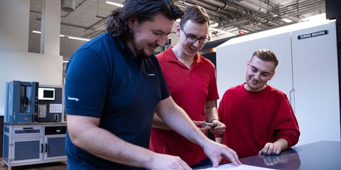 Auszubildender und zwei Azubis stehen an Tisch in der Produktion und besprechen eine Zeichnung