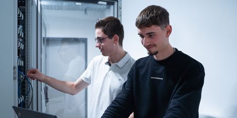 zwei männliche Azubis stehen im Serverraum an Schaltschränken