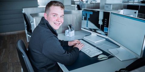 junger Auszubildender sitzt lachend am Schreibtisch am PC